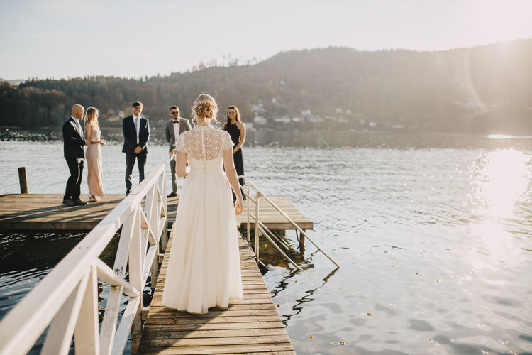 Bride walking on jetty towards groom and friends