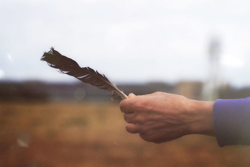 Midsection of man holding feather against sky
