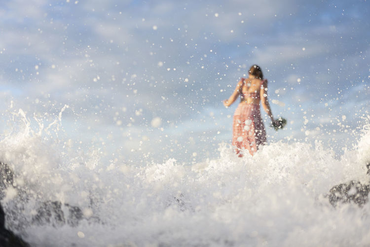 Rear view of woman standing on rock by sea against sky