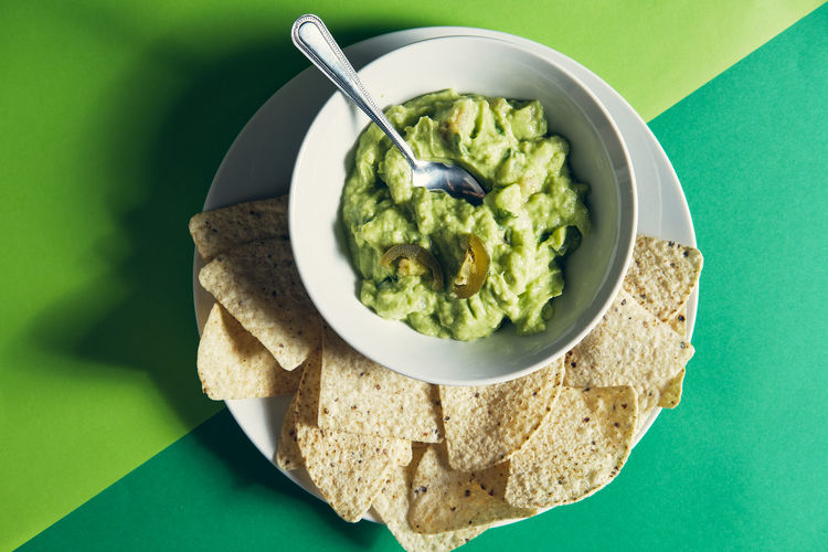 Guacamole sauce in a ceramic bowl on a green background