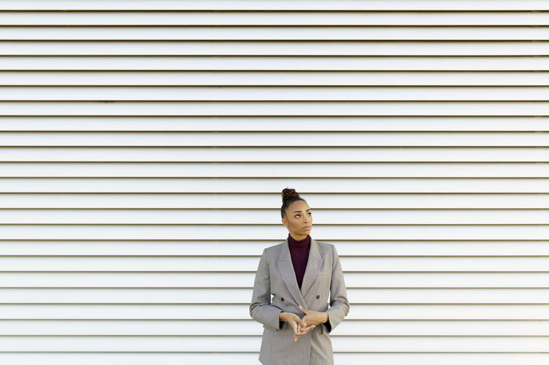 Thoughtful businesswoman looking away while standing against striped wall