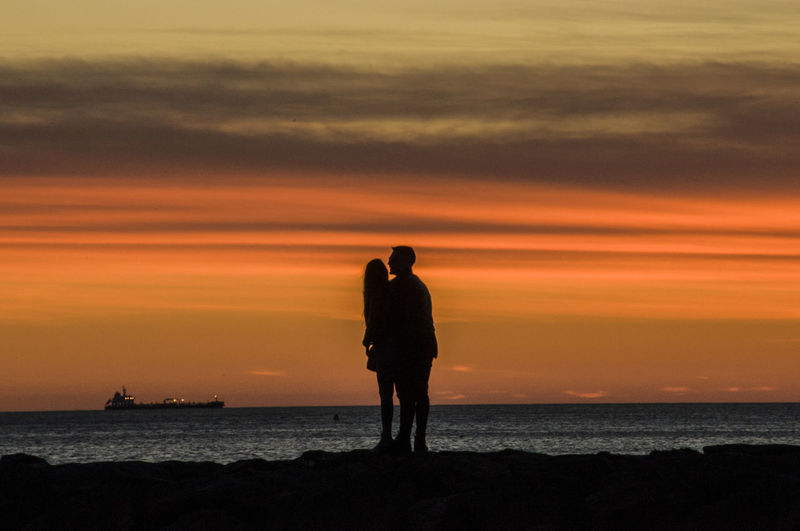 Silhouette couple standing at sea against sky during sunset