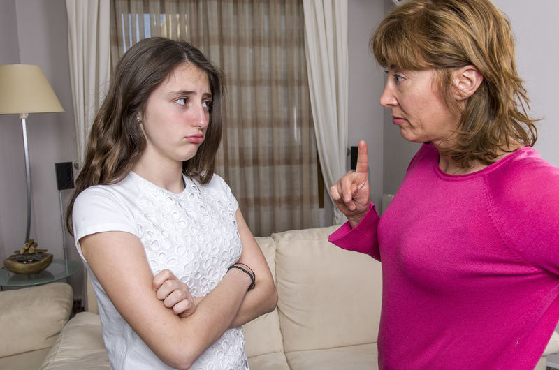 Angry mother scolding daughter while standing in living room at home