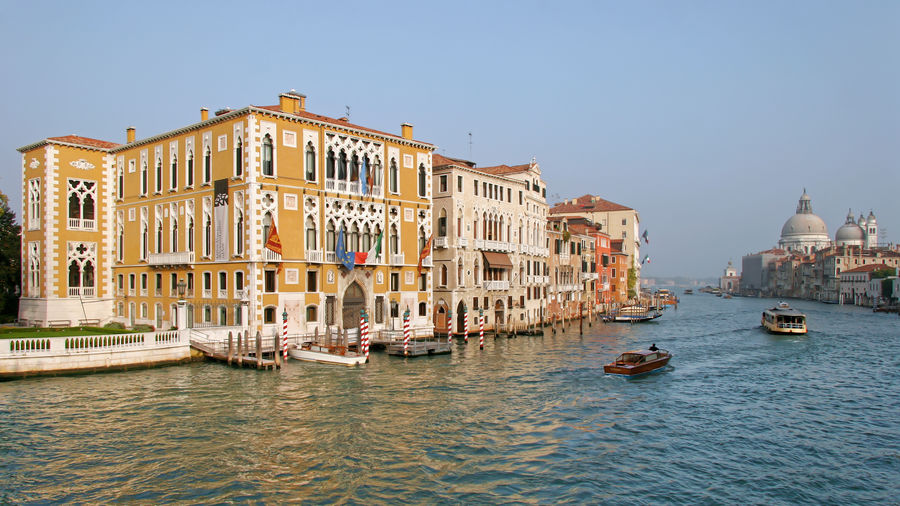 Boats in canal amidst buildings against clear sky