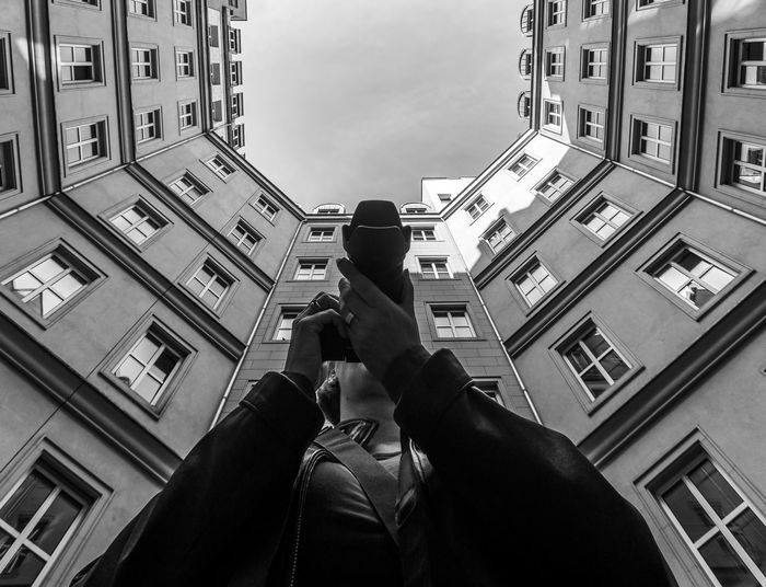 Low angle view of woman photographing against building in city