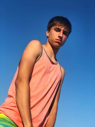 Low angle portrait of young man standing against clear blue sky