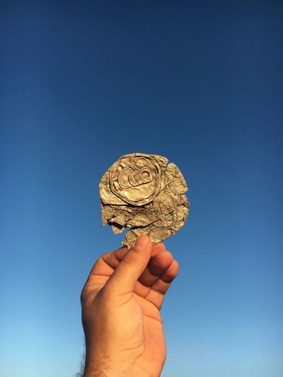 Cropped image of hand holding crushed drink can against clear sky