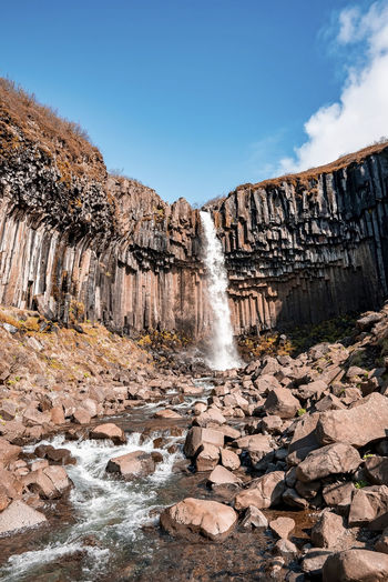 Beautiful cascades of svartifoss waterfall and flowing stream against blue sky