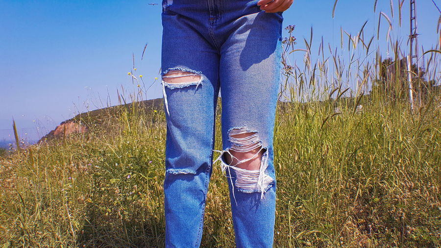 Midsection of woman wearing torn jeans standing by plants on field
