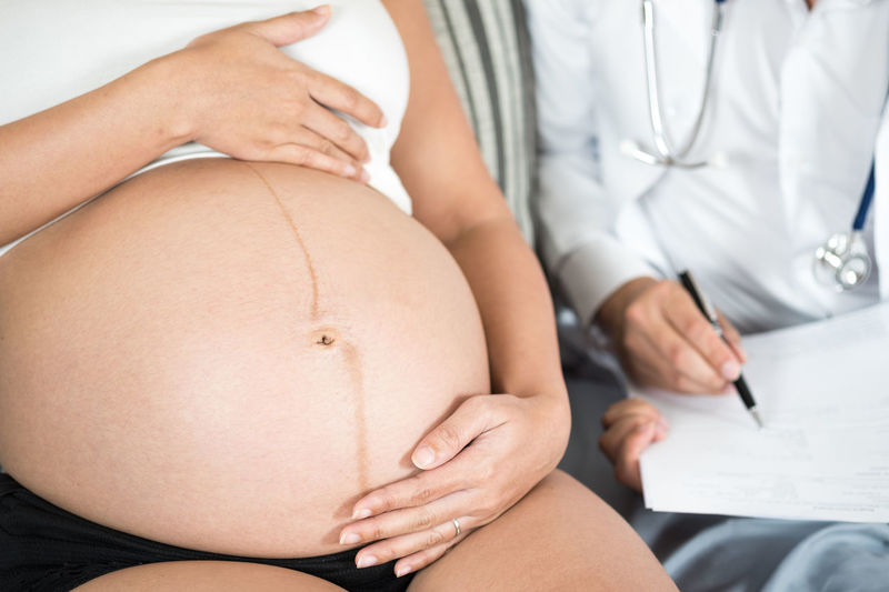 Midsection of pregnant woman sitting with female doctor in hospital