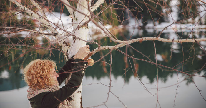 Woman tying christmas ornament on bare tree during winter