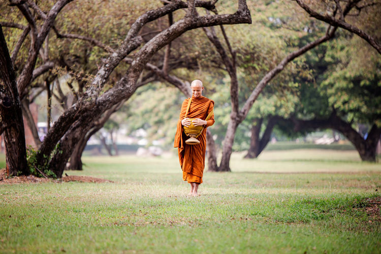 Monk carrying container while walking on land