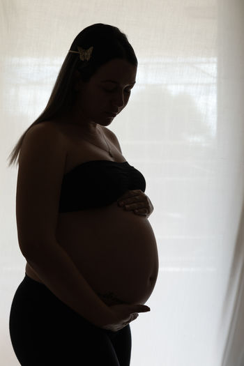 Side view of pregnant woman against clear blinds