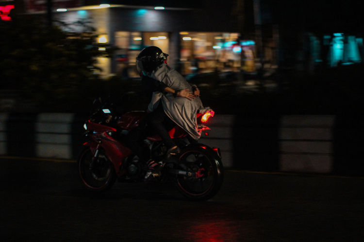 Man riding motorcycle on illuminated street at night