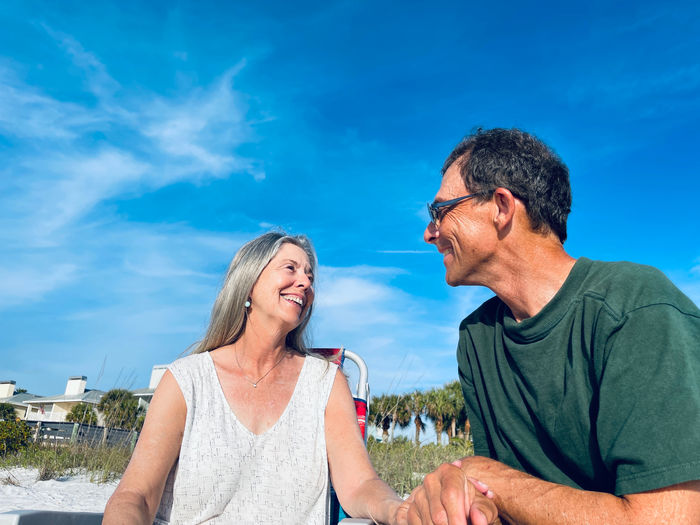 Senior man and woman smiling and looking with love at one another as they sit under blue sky