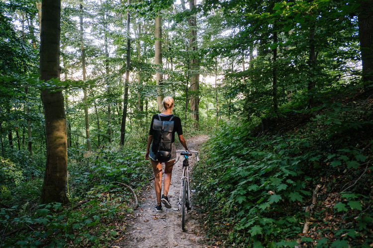 Rear view of woman walking with bicycle on trail in forest