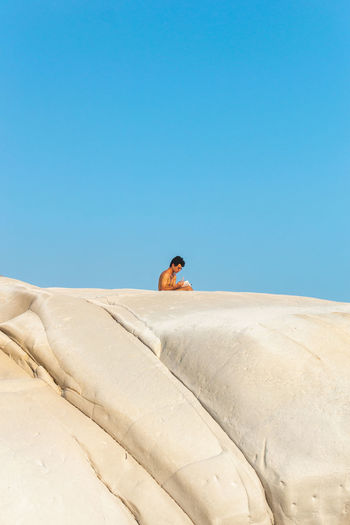 Mid distance view of man sitting against clear blue sky