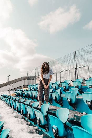 Woman standing on seat against sky