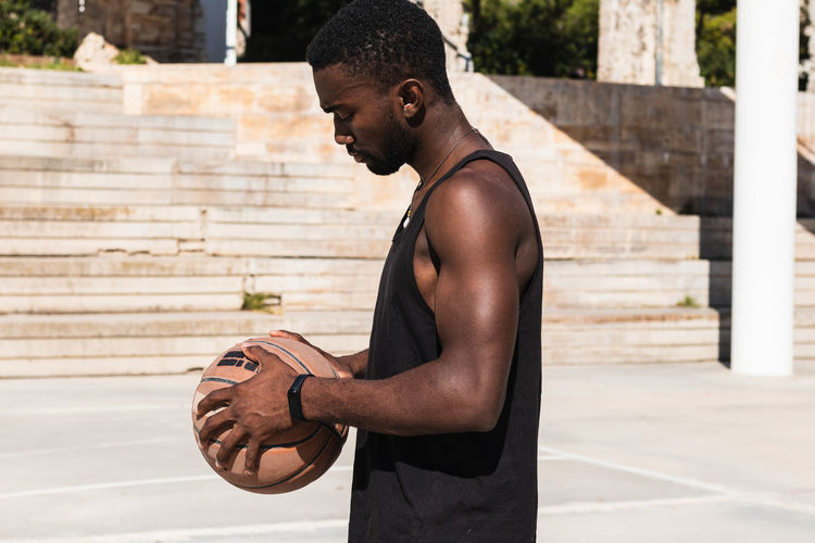 Side view of fit african american male standing on basketball court with ball and looking away