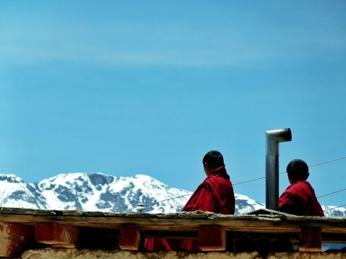 Rear view of monks looking at himalayas against blue sky