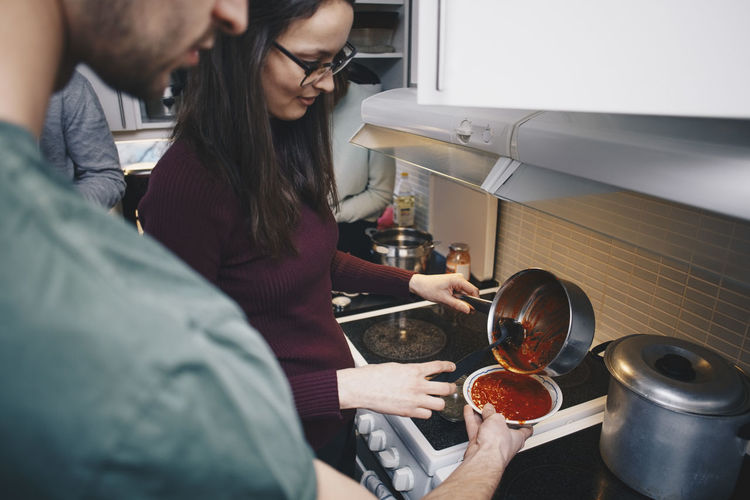 High angle view of woman pouring tomato soup for man holding bowl in kitchen