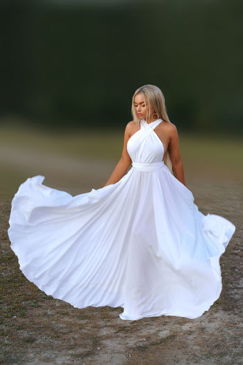Girl, dressed in a snow-white dress, throws her dress aside against the background of nature. 