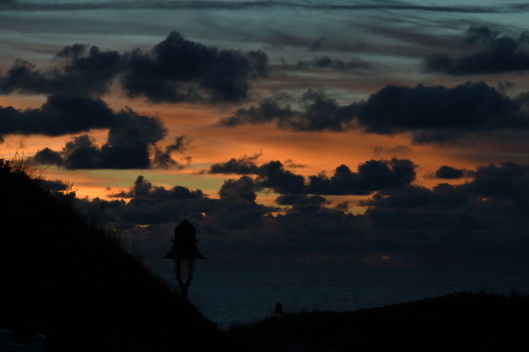 Rear view of silhouette man walking on landscape against sky during sunset