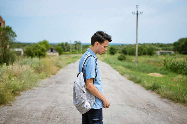 Cute guy with a backpack standing on road in countryside.