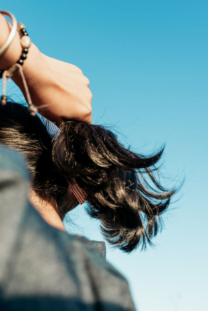 Rear view of woman adjusting hair against clear blue sky