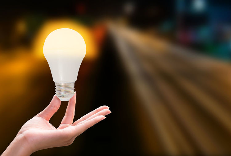 Multiple image of hand holding illuminated light bulb against defocused road