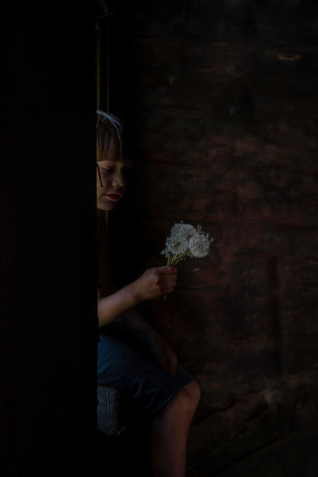 Midsection of kid holding dandelion fluff while sitting in window
