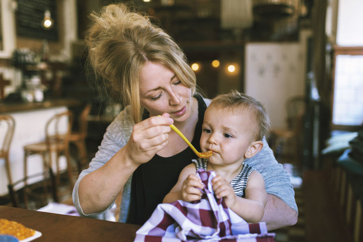 Mid adult mother feeding baby boy at restaurant table