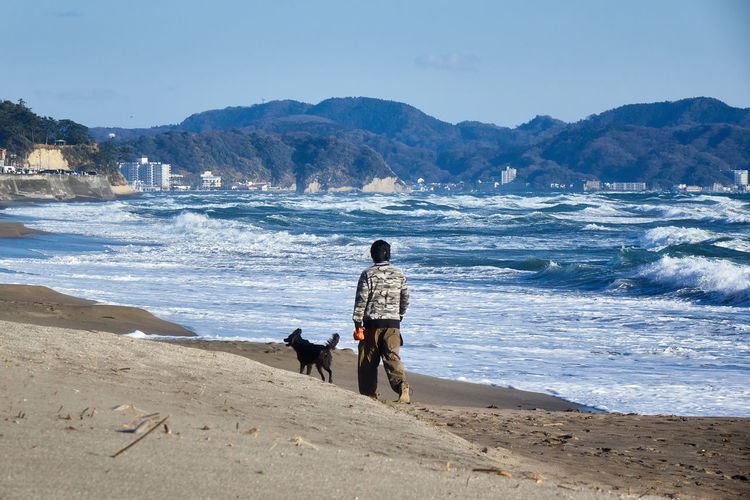 Rear view of man with dog walking at beach
