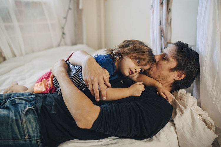 Mature father with eyes closed kissing daughter while lying on bed