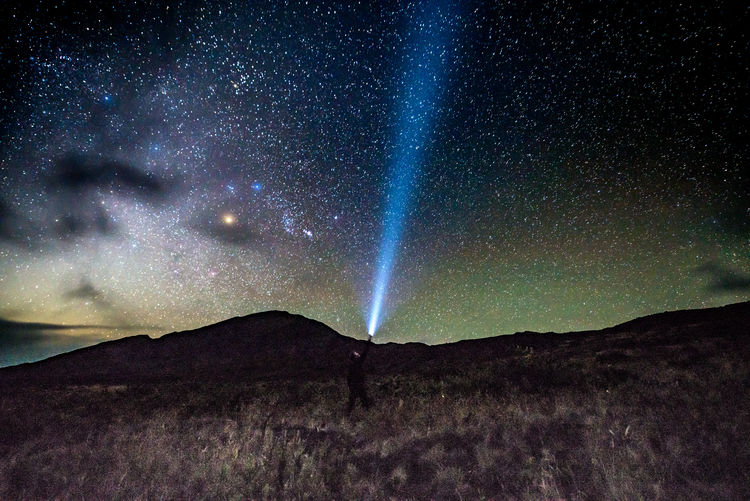 Man with flashlight on mountain against star field