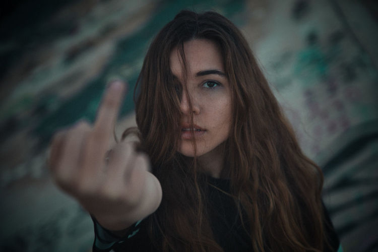 Close-up portrait of young woman making obscene gesture