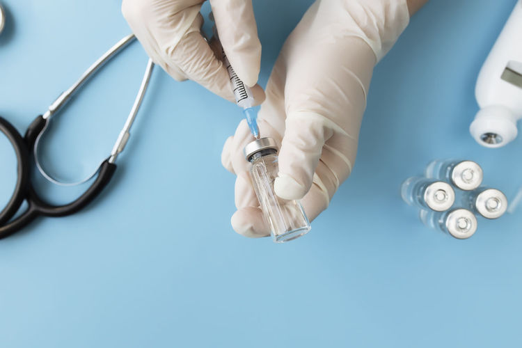 Doctor hands holding bottle with vaccine and injection syringe, and vaccine vial on blue background