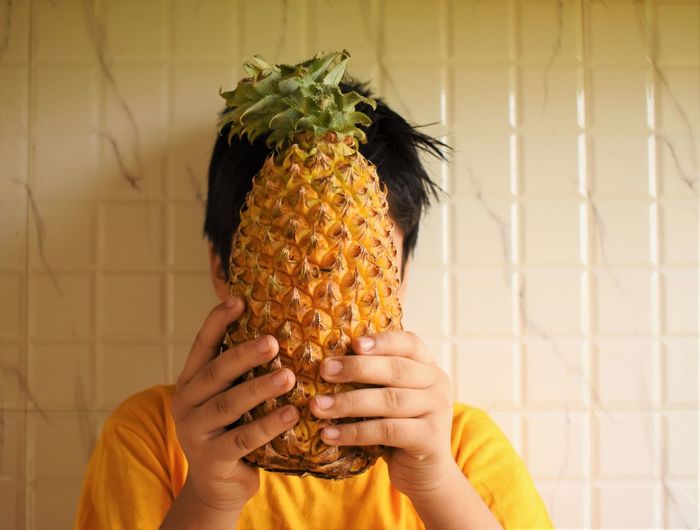 Close-up of boy holding pineapple against his face