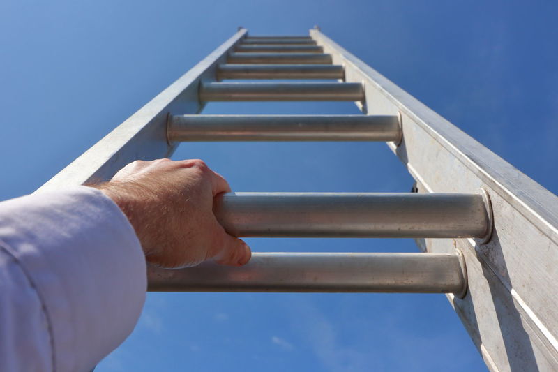Low angle view of man standing on railing against clear blue sky