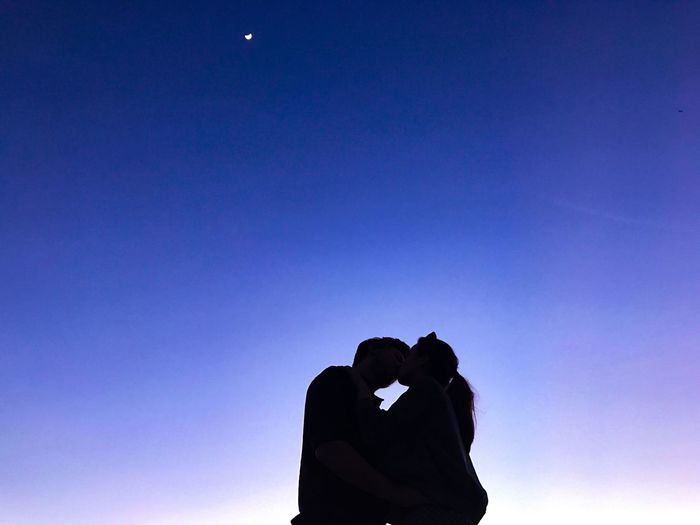 Low angle view of couple kissing while standing against blue sky during sunset