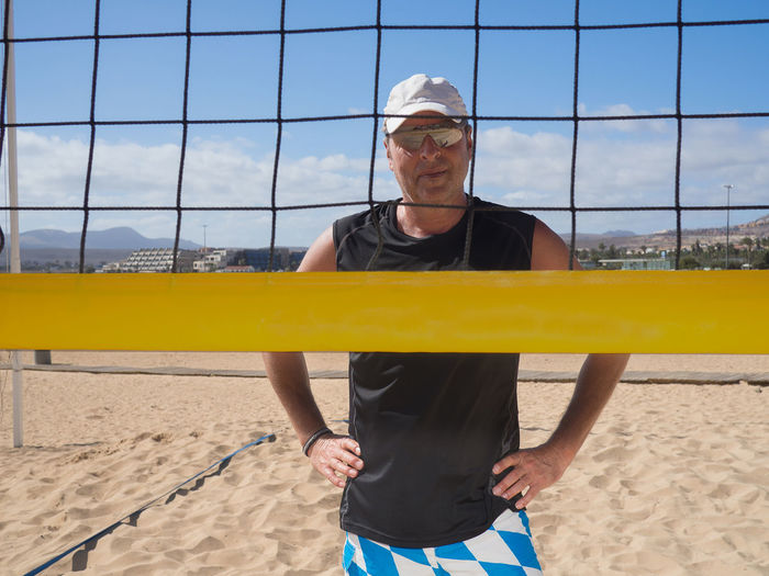 Portrait of man in sunglasses standing by volleyball net against sky