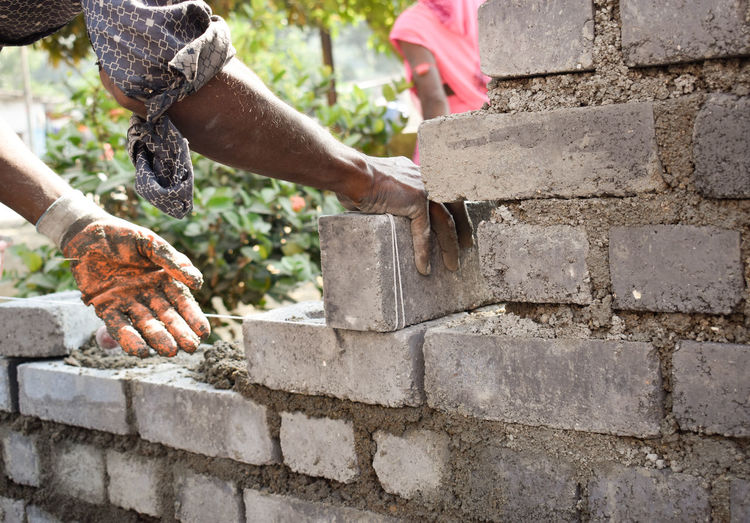 Man holding laying bricks and building fly ash  brick wall in india