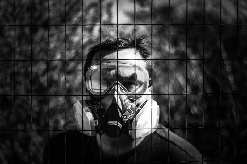 Portrait of man wearing mask seen through fence