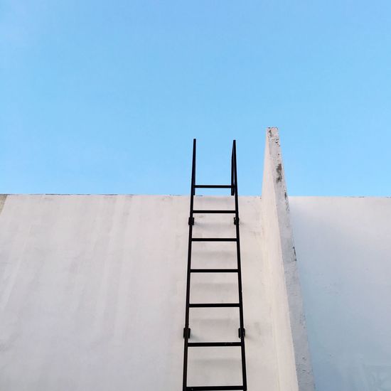 Low angle view of ladder on concrete wall against clear blue sky