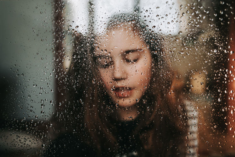 Close-up of girl seen through wet window in rainy season