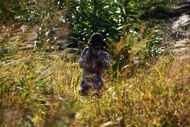 Woman photographing amidst plants in forest