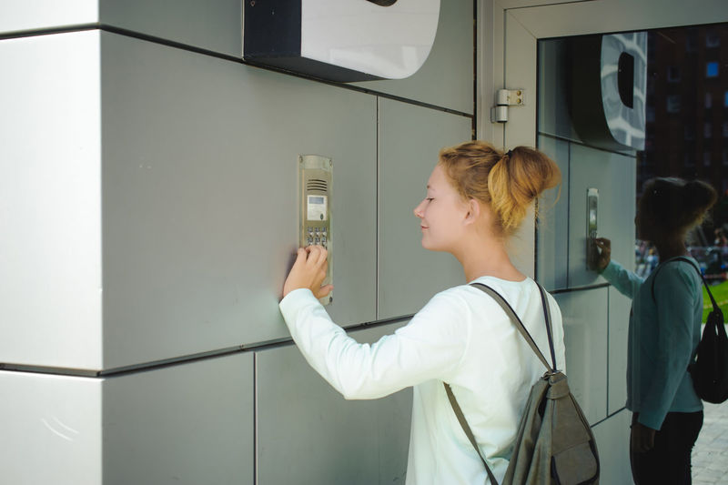 Side view of young woman using intercom