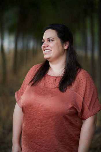 Cheerful young chubby female in casual apparel looking away with toothy smile in daylight
