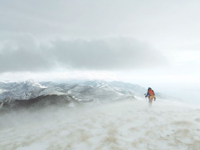 Hiker standing on snowcapped mountain against sky
