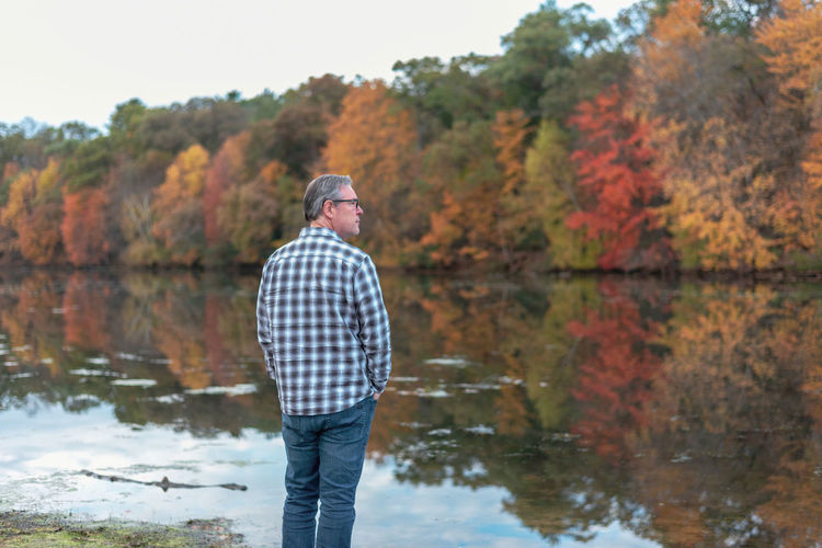 Rear view of man standing by lake during autumn